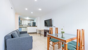 A modern living room with a sofa, dining table, chairs, and a TV. - Spain Breaks - 2 bed apt With 2 Pools, Airco, Wifi (Benalmádena)