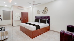 A modern bedroom with a wooden bed, a ceiling fan, a round mirror, and decorative wall art. - Deluxe With Twin Bedthe Paradise Guest inn (Nellore)