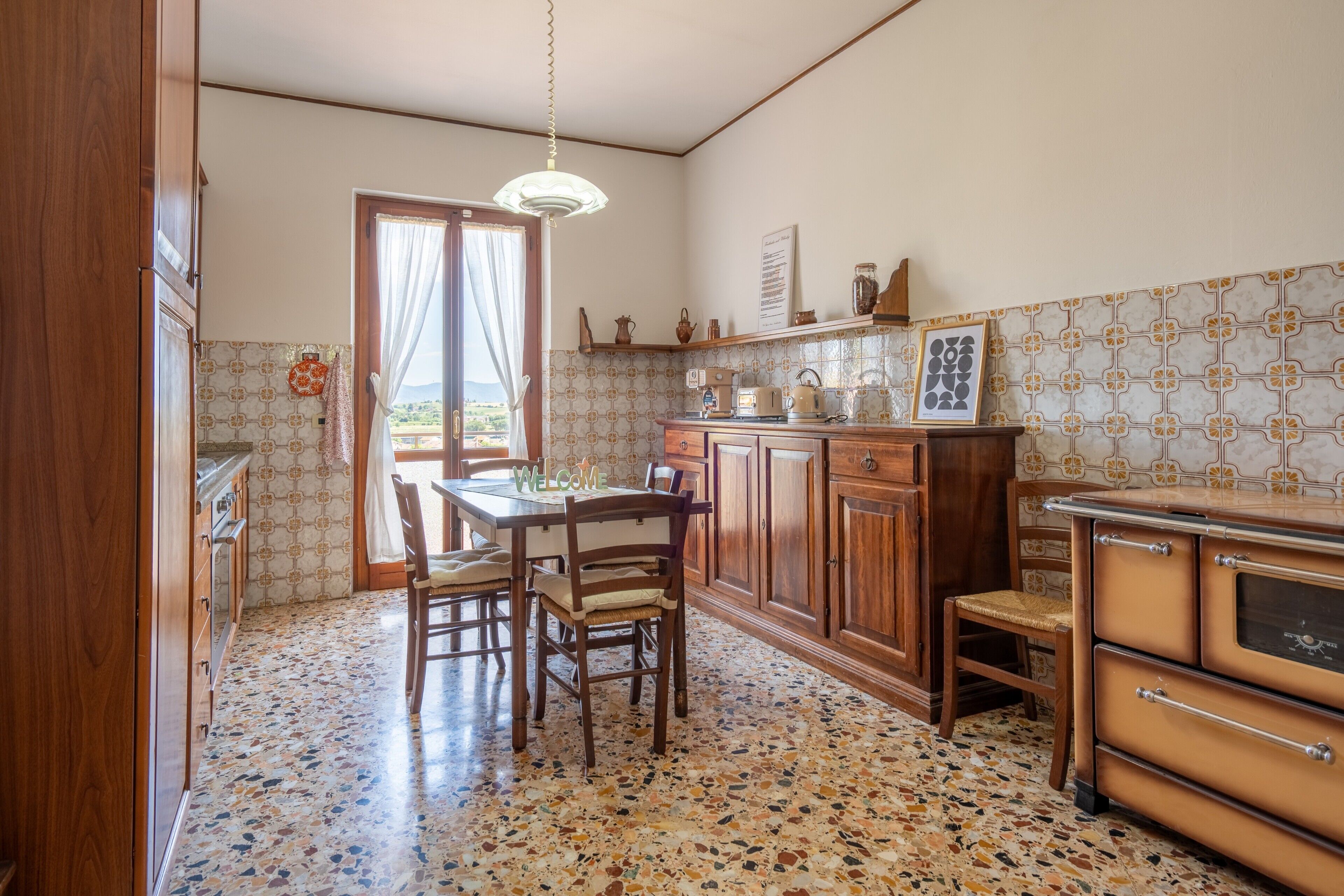 Una cocina con mesa y sillas, armarios de madera, una encimera y suelo estampado.