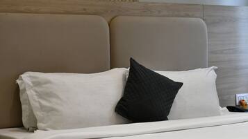 Una cama con ropa blanca y almohada negra, cabecera de madera y un objeto amarillo pequeño en la mesita de noche.