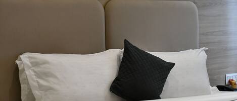 A bed with white bedding and a black pillow, a wooden headboard, and a small yellow object on the nightstand.