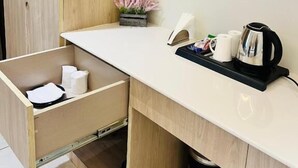 Eine kleine Küchenzeile mit einer Arbeitsplatte, einer Kaffeemaschine, einer Ablage mit Tassen und einem Mülleimer.