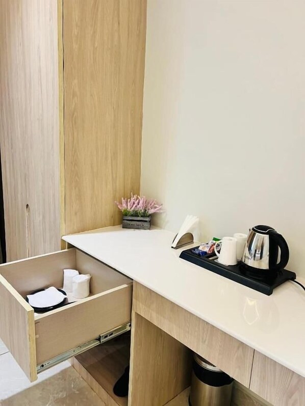 A small kitchenette with a countertop, a coffee maker, a tray with cups, and a trash bin.