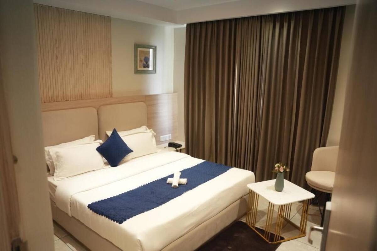 A hotel room with a bed, a bedside table, a chair, and a curtain.