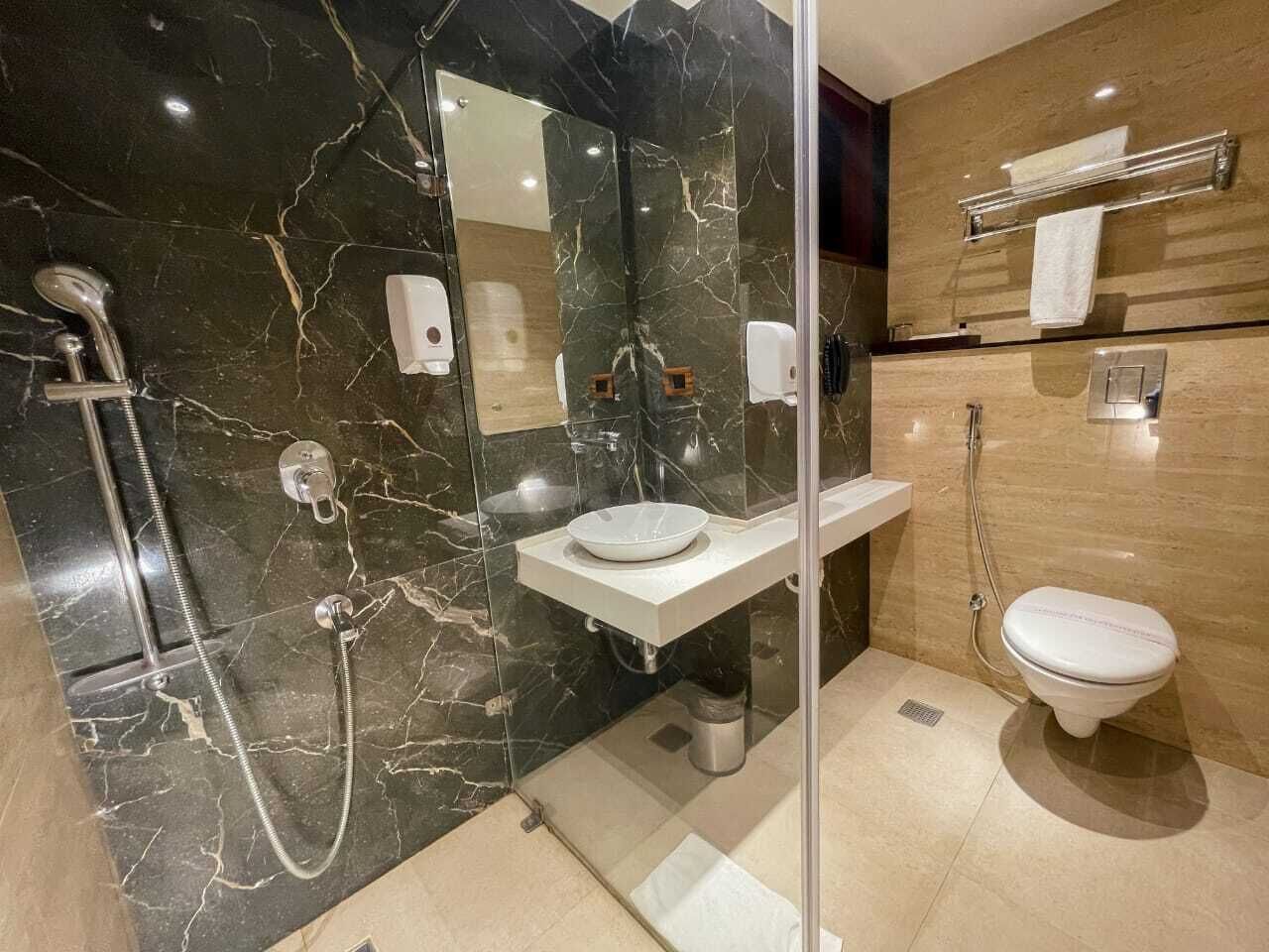 A modern bathroom with a marble shower, a sink with a mirror, and a toilet.