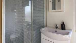 Ein Badezimmer mit Duschkabine aus Glas, einem weißen Waschbecken mit Spiegel darüber und einem schwarzen Seifenspender.