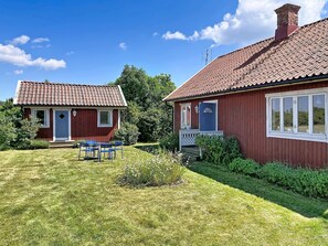 Ett rött trähus med ett tak täckt av tegelpannor, en veranda med stolar och en välskött gräsmatta.