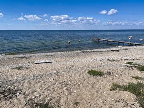 A rocky beach with a wooden pier extending into calm water, a lifebuoy, and sparse vegetation. - Villa Alvaret by Interhome (Borgholm)