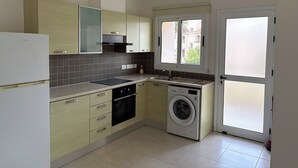 Una cucina compatta con lavatrice integrata, frigorifero e una finestra con vetro acidato.