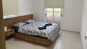 Camera da letto con un letto in legno, un comodino, una finestra con persiana e una porta scorrevole verso un balcone.