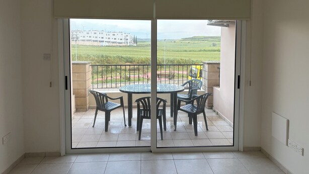 Un balcone con tavolo e sedie, vista su un edificio e un campo erboso.