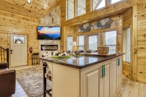 Ein Holzblockhaus-Innenraum mit Kücheninsel, Kamin und großem Fenster mit Jalousien.