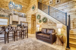 A wooden interior with a kitchen, bar area, leather sofa, and a staircase. - Pigeon Forge Luxury Cabin w/ Private Bowling Alley & Hot Tub (Sevierville)