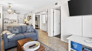 Un salon moderne avec un canapé, un pouf et un téléviseur à écran plat.