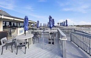 An outdoor deck with tables and chairs, blue umbrellas, and a sign for a beach club. - Tennis Villa G6 - 2BR Beach Retreat Walk to Beach (Hilton Head Island)