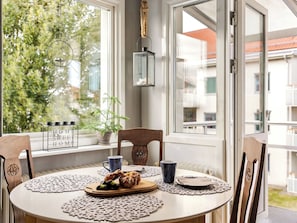 A dining area with a table set for two, a potted plant, and a view of a residential building.