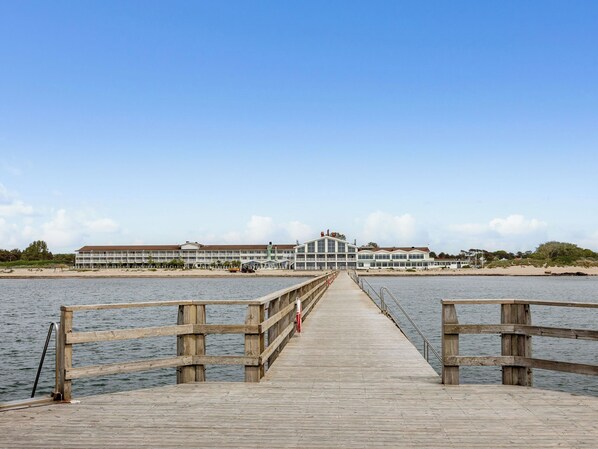 A wooden pier leading to a beachfront hotel with multiple buildings and a sandy beach.