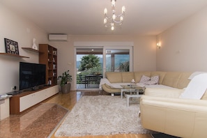 A living room with a sofa, TV, bookshelf, and a potted plant. - Holiday Home Vele with pool (Vrgorac)