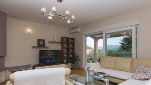 A living room with a sofa, a glass coffee table, a TV, a bookshelf, and a chandelier. - Holiday Home Vele with pool (Vrgorac)