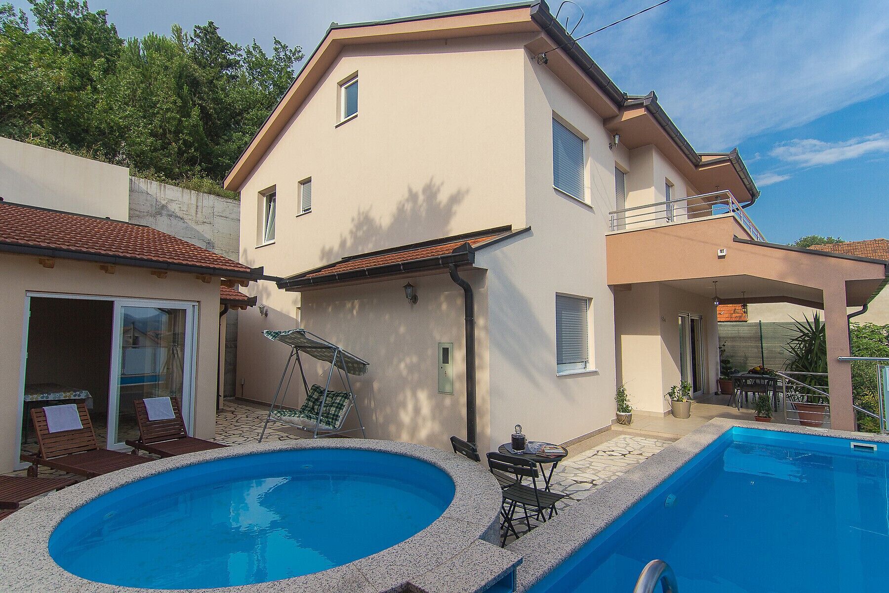 A two-story house with a swimming pool, outdoor seating, and a balcony.