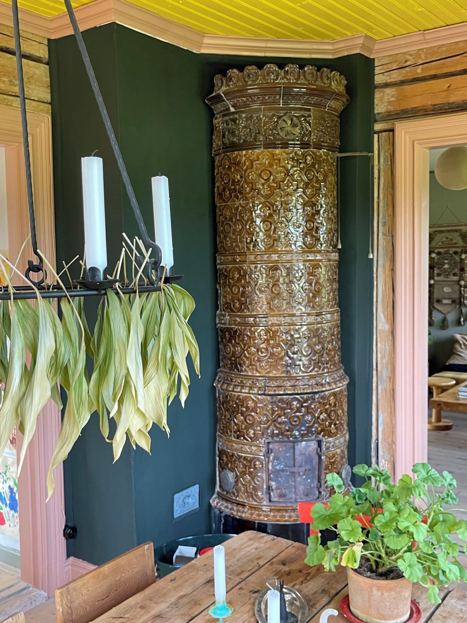 A room with a wooden table, a green wall, a decorative column, and hanging dried leaves.