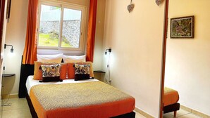 A bedroom with a bed, curtains, a window, a bedside table, a lamp, and a picture on the wall. - Lodge with shared pool - 4 guests (Le Tampon)
