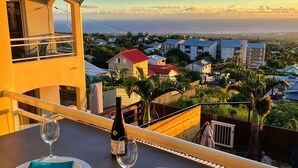 A balcony with a table set for two, overlooking a residential area with houses and a view of the sea. - Peaceful lodging in Tampon, ocean view - 2 guests (Le Tampon)