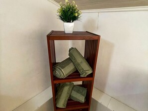 Ein Holzregal mit einer Topfpflanze und gefalteten Handtüchern.