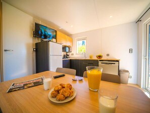 A compact kitchen with a TV, a dining table with food and drinks, and a window with a view. - Cottage with AC, pets allowed - 6 guests (Balaruc-les-Bains)
