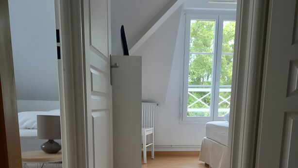 Una habitación con techo inclinado, cama, sillón y ventana con vistas al verdor.