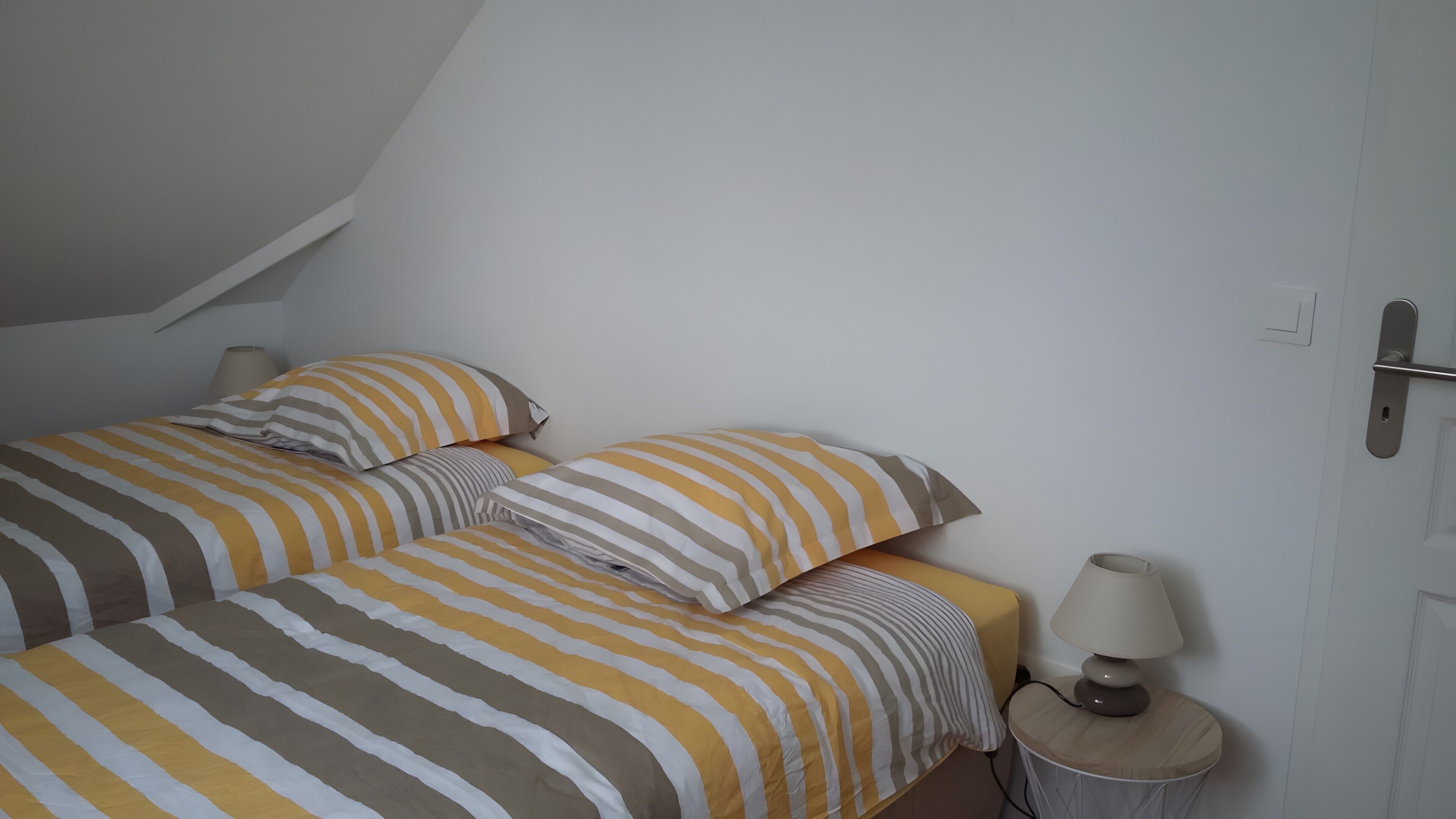 A bedroom with two beds, striped bedding, a bedside lamp, and a door with a handle.