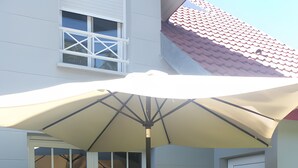 Un patio con una mesa y sillas, un paraguas grande y una puerta corrediza de vidrio que da a un espacio al aire libre.