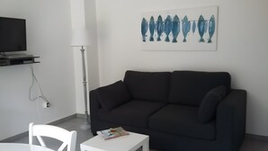 Un salón moderno con un sofá oscuro, una mesita auxiliar blanca y una obra de arte en la pared con motivos de peces.
