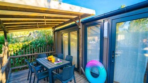 A covered patio with a table and chairs, a sliding glass door, and a colorful inflatable ring. - Spacious cottage with AC - 8 guests (Balaruc-les-Bains)