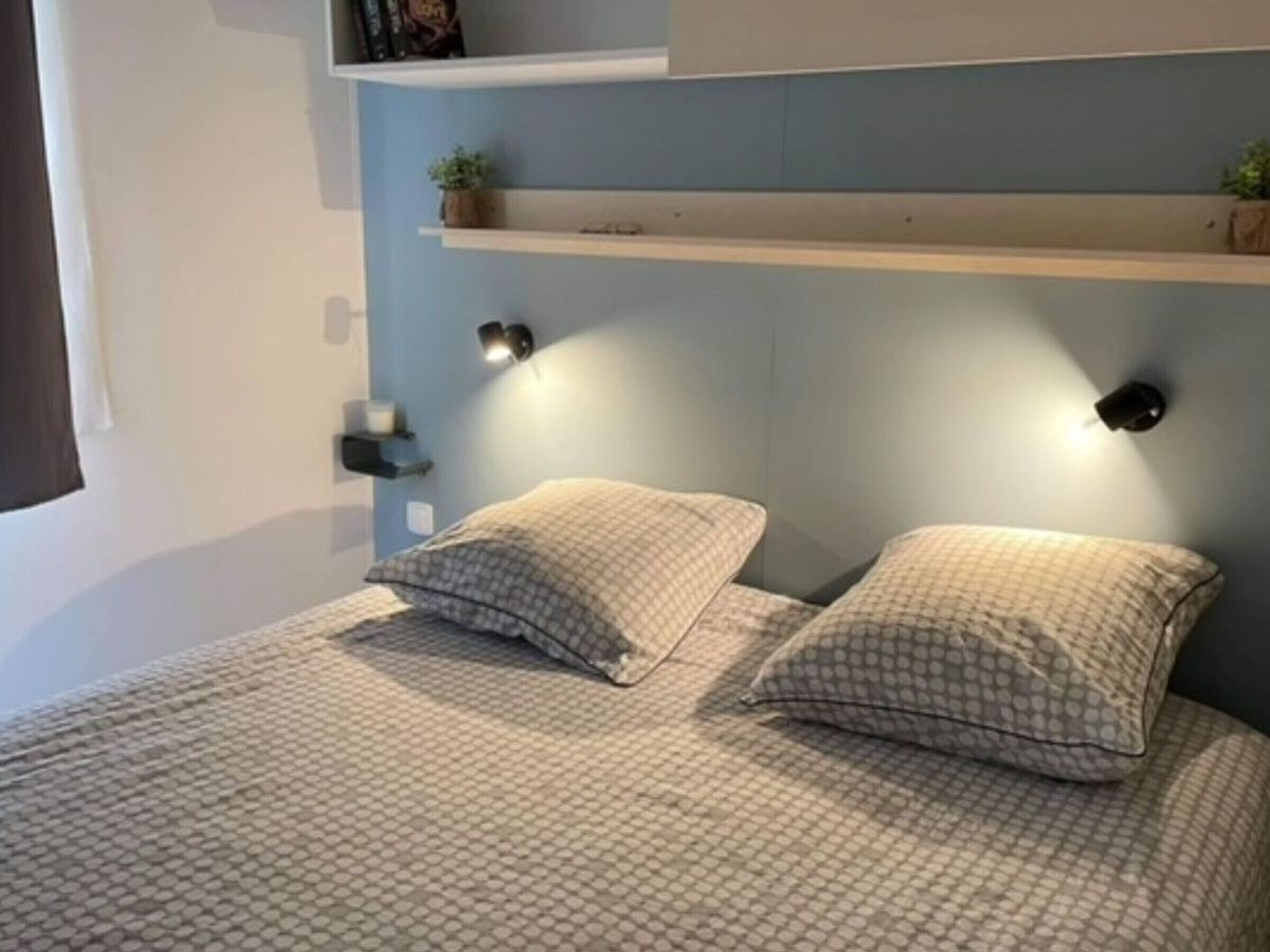Ein Schlafzimmer mit einem Bett, zwei Kissen, einem Nachttisch, einem Bücherregal und Wandleuchten.