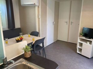 Eine kleine Küchenzeile mit Spüle, ein kleiner Esstisch mit Stühlen, einer Obstschale und einem Fernseher auf einem Schrank.