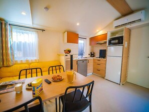 A compact kitchen with a dining area, a sofa, and a small table with food and drinks. - Air-conditioned mobile home - 4 guests (Balaruc-les-Bains)
