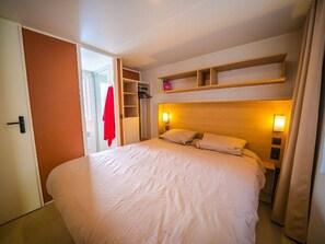 Een hotelkamer met een groot bed, een garderobe, een plank boven het bed en een deur naar een andere kamer.