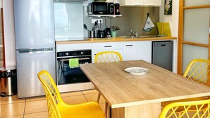 Kompakti keittiö, jossa on jääkaappi, uuni, mikroaaltouuni ja astianpesukone. Keittiössä on ruokapöytä tuoleineen sekä pieni hylly tiskialtaan yläpuolella.