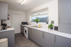 A modern kitchen with a built-in washing machine, a window with blinds, and a sink. - Vacant Nests | The Freda | Modern 3BR Home | (Sunderland)