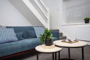 A modern living room with a blue sofa, two round tables, and a potted plant. - Vacant Nests | The Freda | Modern 3BR Home | (Sunderland)