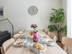 Una mesa de comedor con alimentos para el desayuno, un reloj y una planta en maceta.
