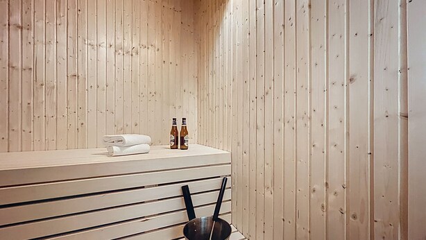 Un sauna de madera con un banco, dos botellas y una toalla.