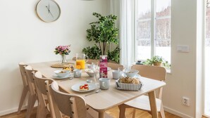 Un comedor con una mesa dispuesta para el desayuno, que incluye una jarra de zumo de naranja, una hogaza de pan y diversas opciones para el desayuno.