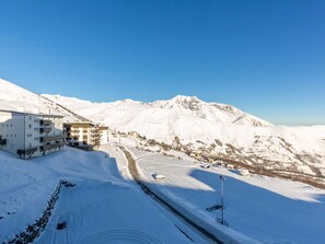 Schneebedeckte Landschaft mit einem mehrstöckigen Gebäude mit Balkonen, umgeben von Bergen und wolkenlosem Himmel.
