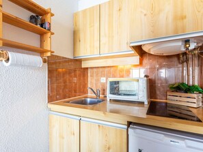 Eine kleine Küche mit Holzausstattung, einer integrierten Mikrowelle, einem Spülbecken und einem Geschirrspüler.