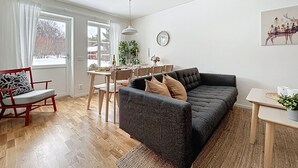 Una sala de estar moderna con un sofá gris oscuro, una mesa de comedor de madera y una pequeña mesita auxiliar.