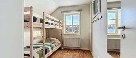 A small room with bunk beds, a window with a view, a radiator, and a door with a handle.