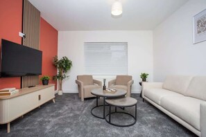 Una sala de estar moderna con un sofá, dos sillones, una mesa de centro, un televisor y una ventana con persianas.