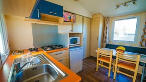 A compact kitchen with a sink, stove, microwave, and a dining area with chairs and a table. - Mobile-home with AC - 4 guests (Frontignan)